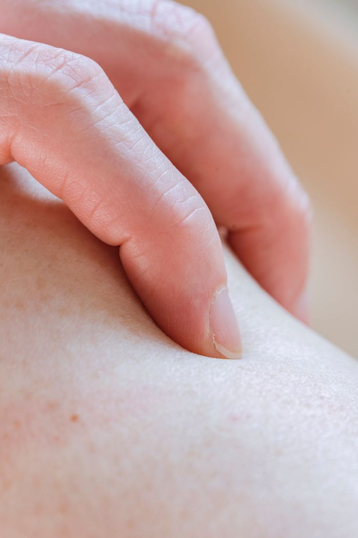 Closeup of crop anonymous person touching delicate skin of leg with hand while standing in light room on blurred background