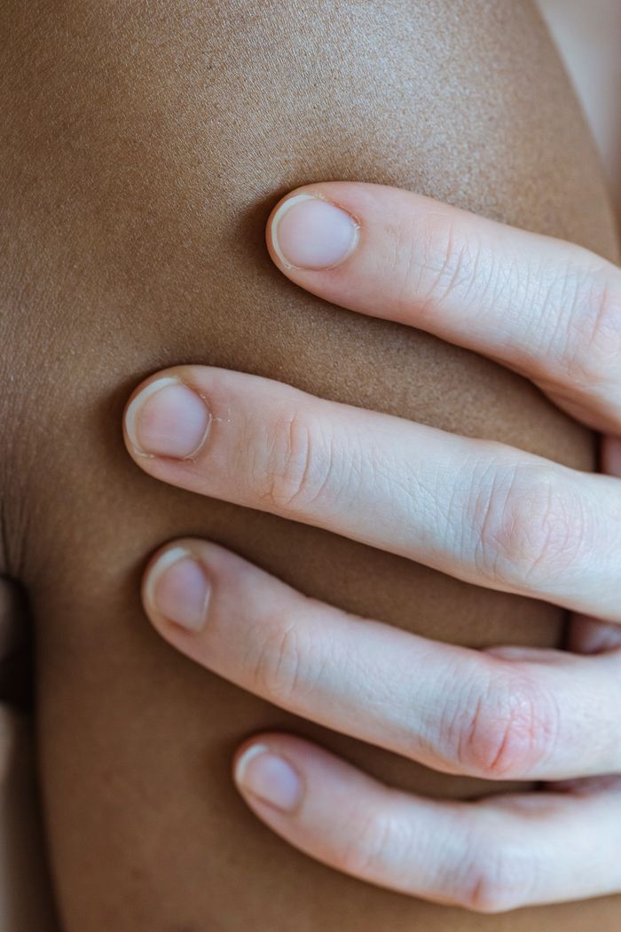 Closeup of crop faceless person touching arm of anonymous African American person with smooth skin in light room at home
